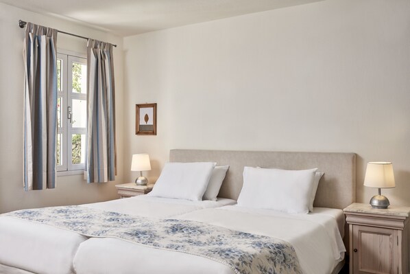 Una cama doble con colcha estampada, dos lámparas de noche y una ventana con cortinas.