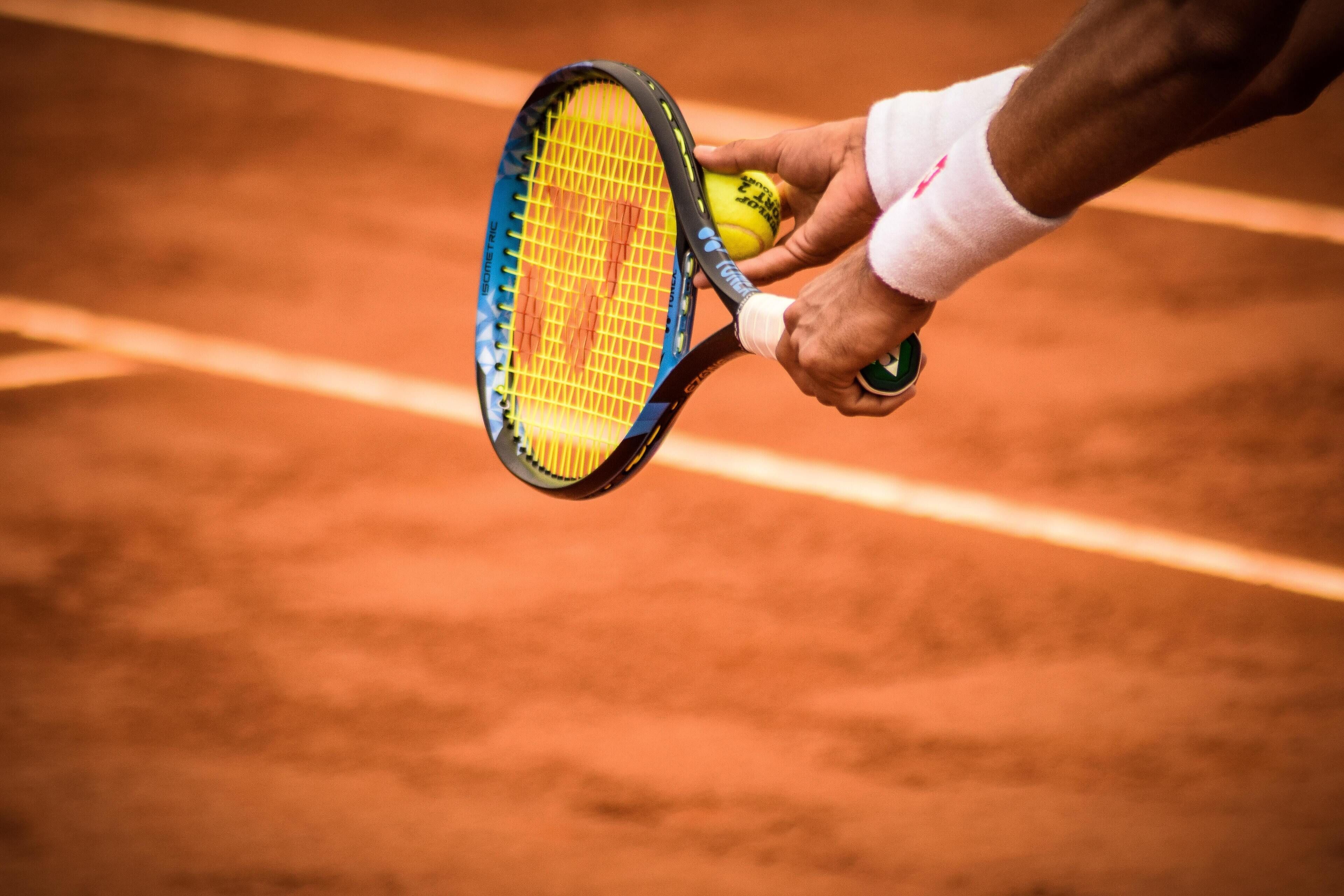 Una racchetta da tennis e una pallina su un campo in terra rossa.