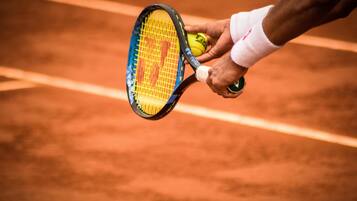 Una racchetta da tennis e una pallina su un campo in terra rossa.