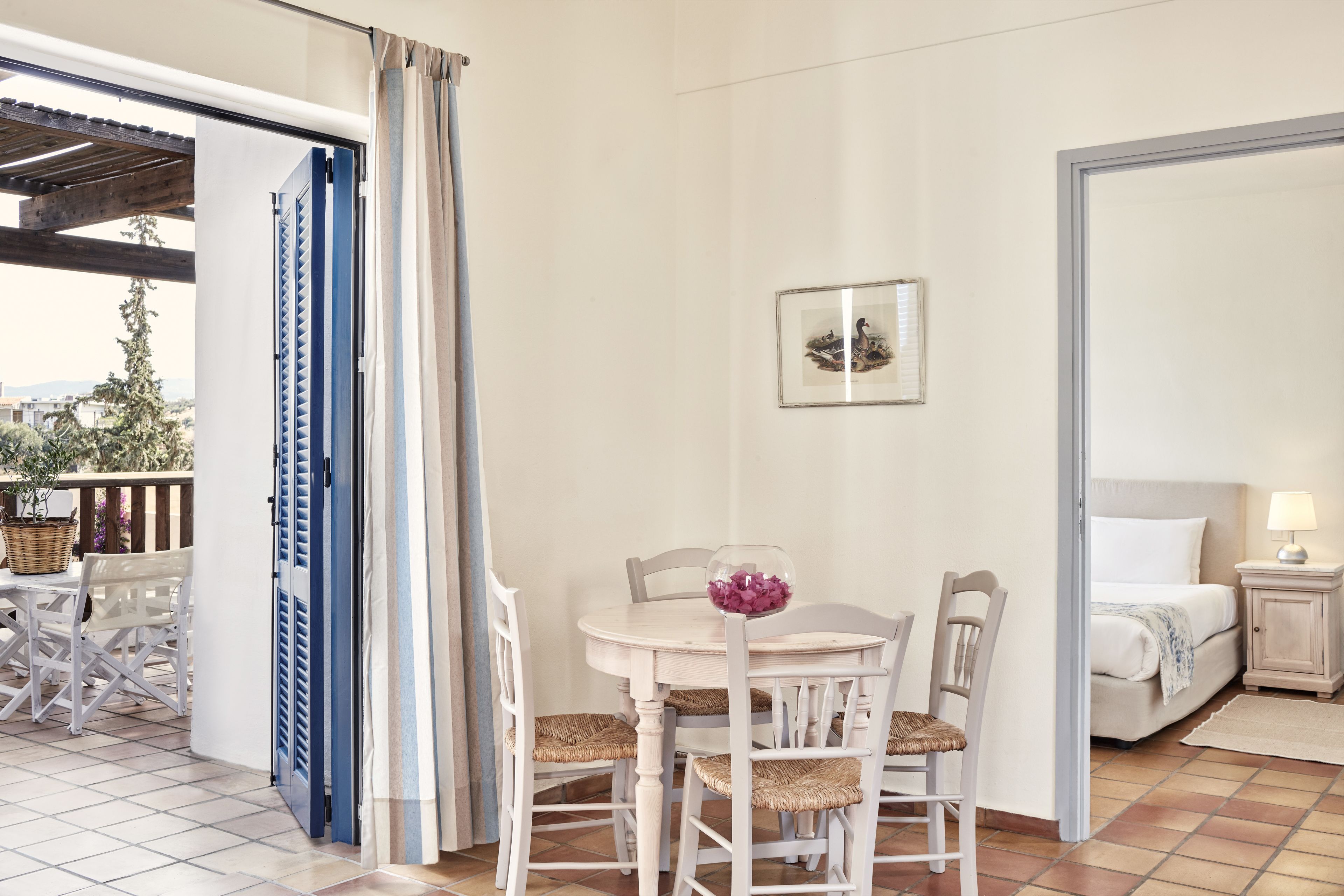 Una habitación con una mesa de comedor, sillas, una cama y una pequeña mesita de noche con una lámpara.
