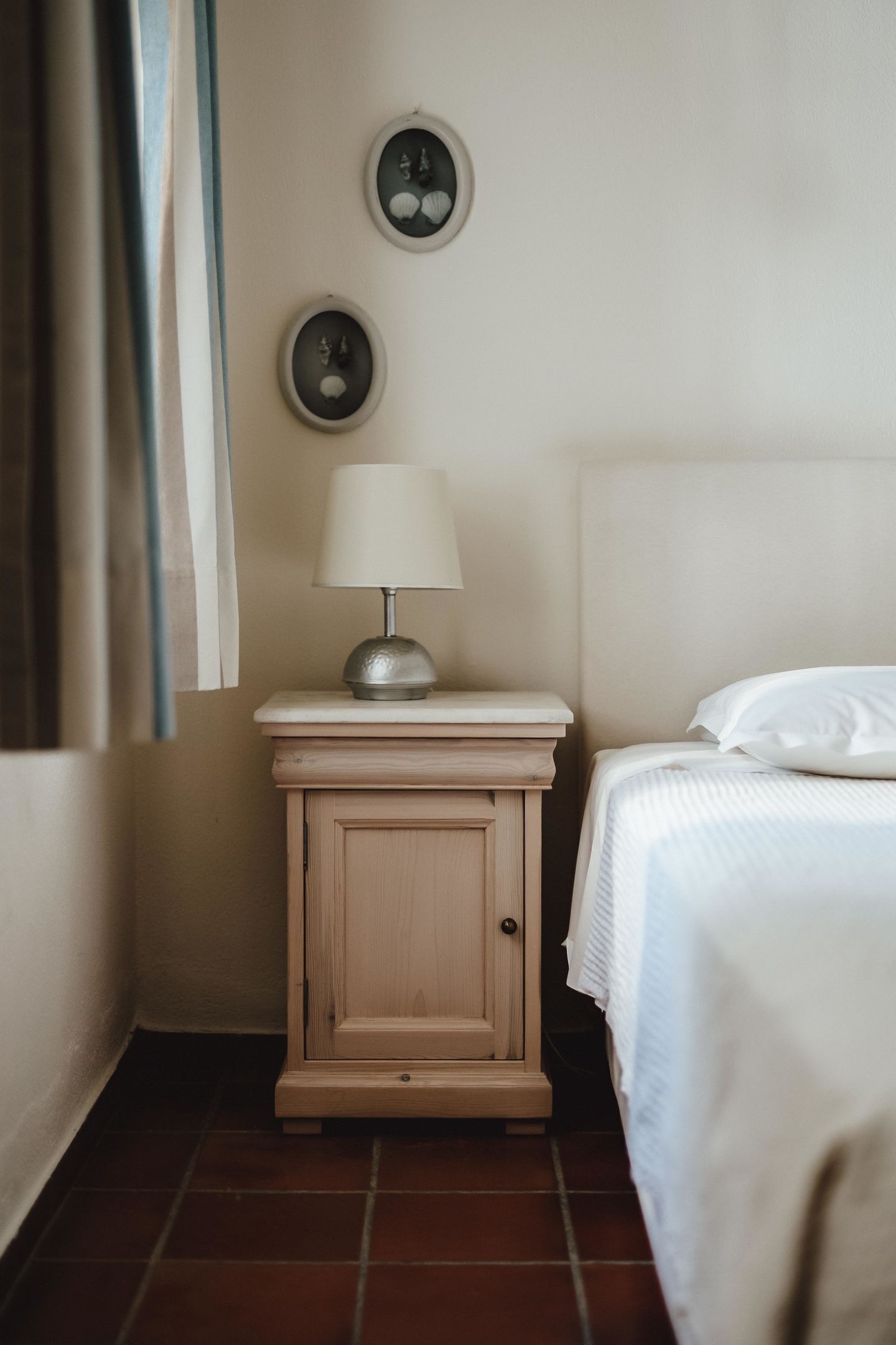 Une petite chambre à coucher, bien rangée, avec un lit simple, une table de chevet avec une lampe et deux cadres photos accrochés au mur.