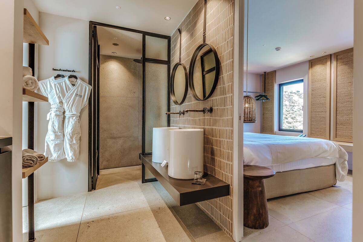 A modern bathroom with a walk-in shower, a large mirror, and a bed with a view of the outdoors.