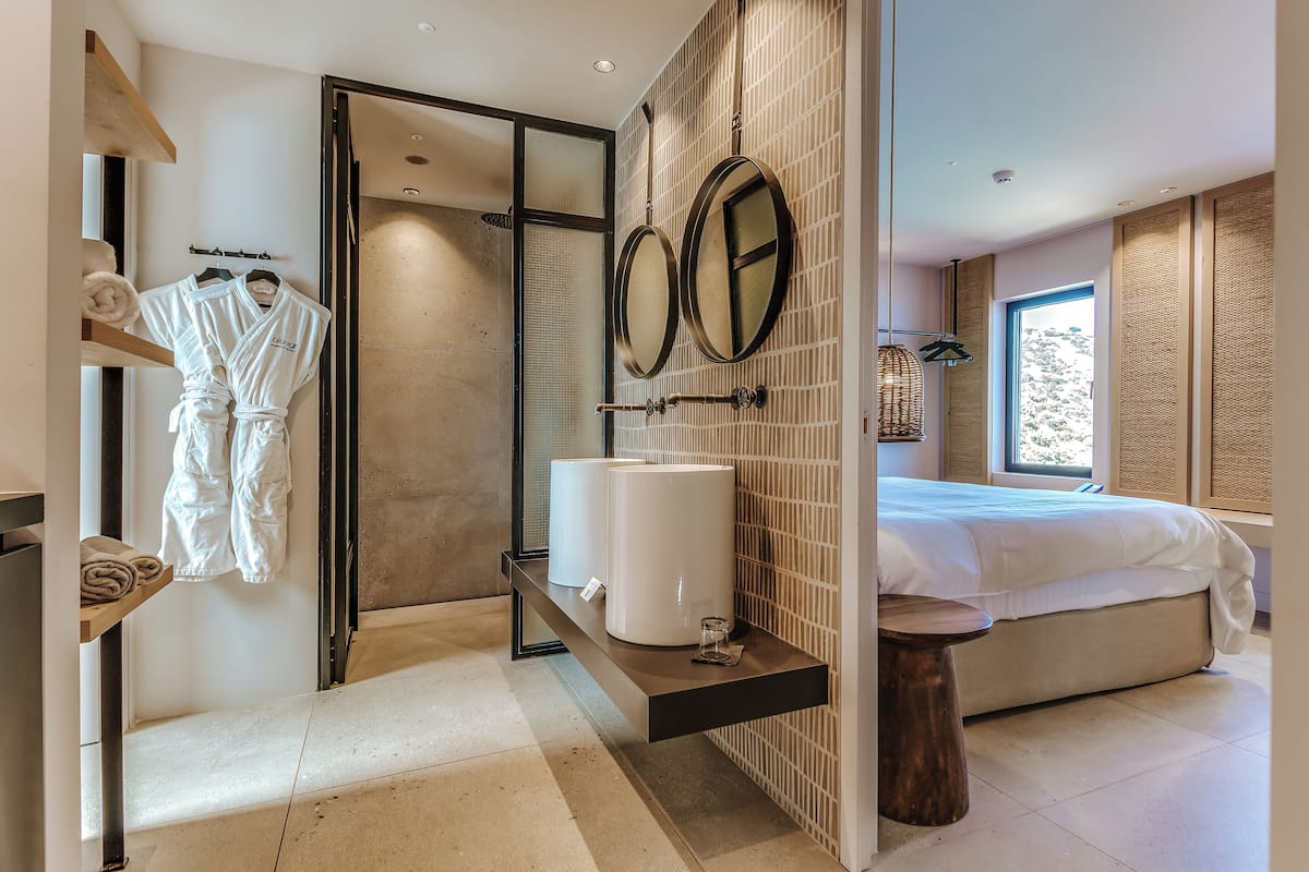 A modern bathroom with a walk-in shower, a large mirror, and a bed with a view of the outdoors.