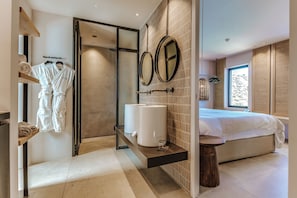 A modern bathroom with a walk-in shower, a large mirror, and a bed with a view of the outdoors. - Candia Park Village (Agios Nikolaos)