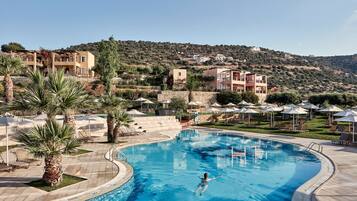 Ein Swimmingpool mit einer Person, umgeben von Palmen und Liegestühlen.