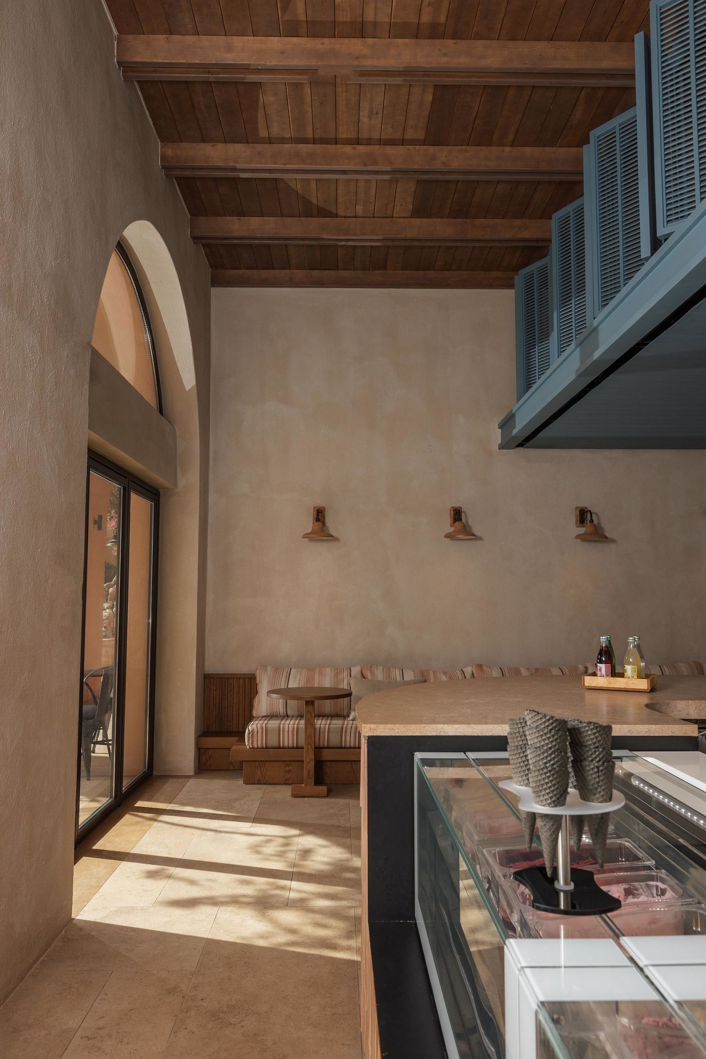 Een modern interieur met een houten plafond, een glazen vitrine met etenswaren en een zithoek met een bank en gestoffeerde stoelen.