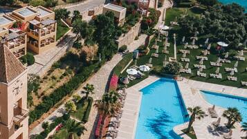 A resort with multiple buildings, a central swimming pool, and a view of the sea.