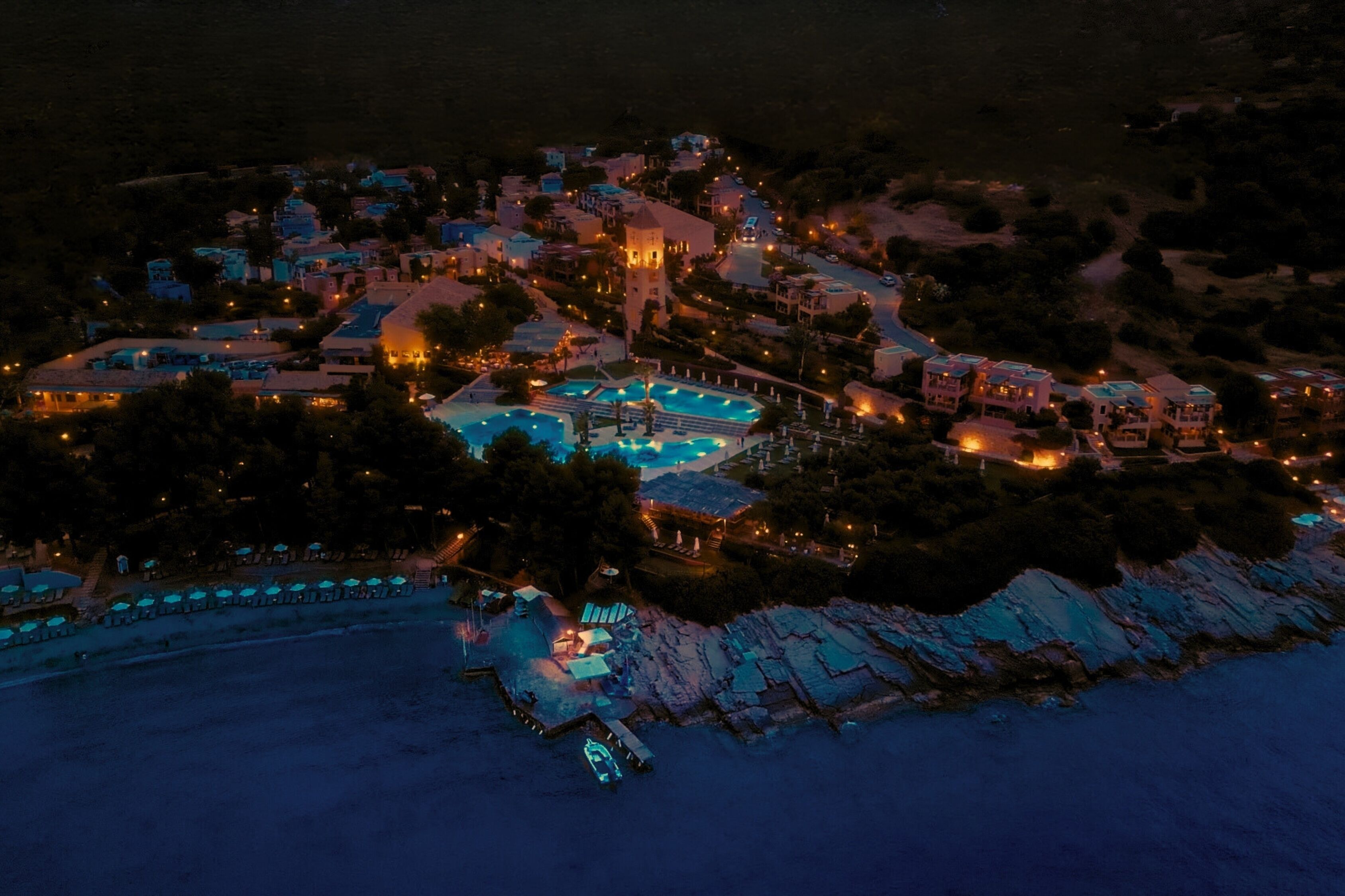 An aerial view of a coastal resort with multiple buildings, a swimming pool, and a dock.