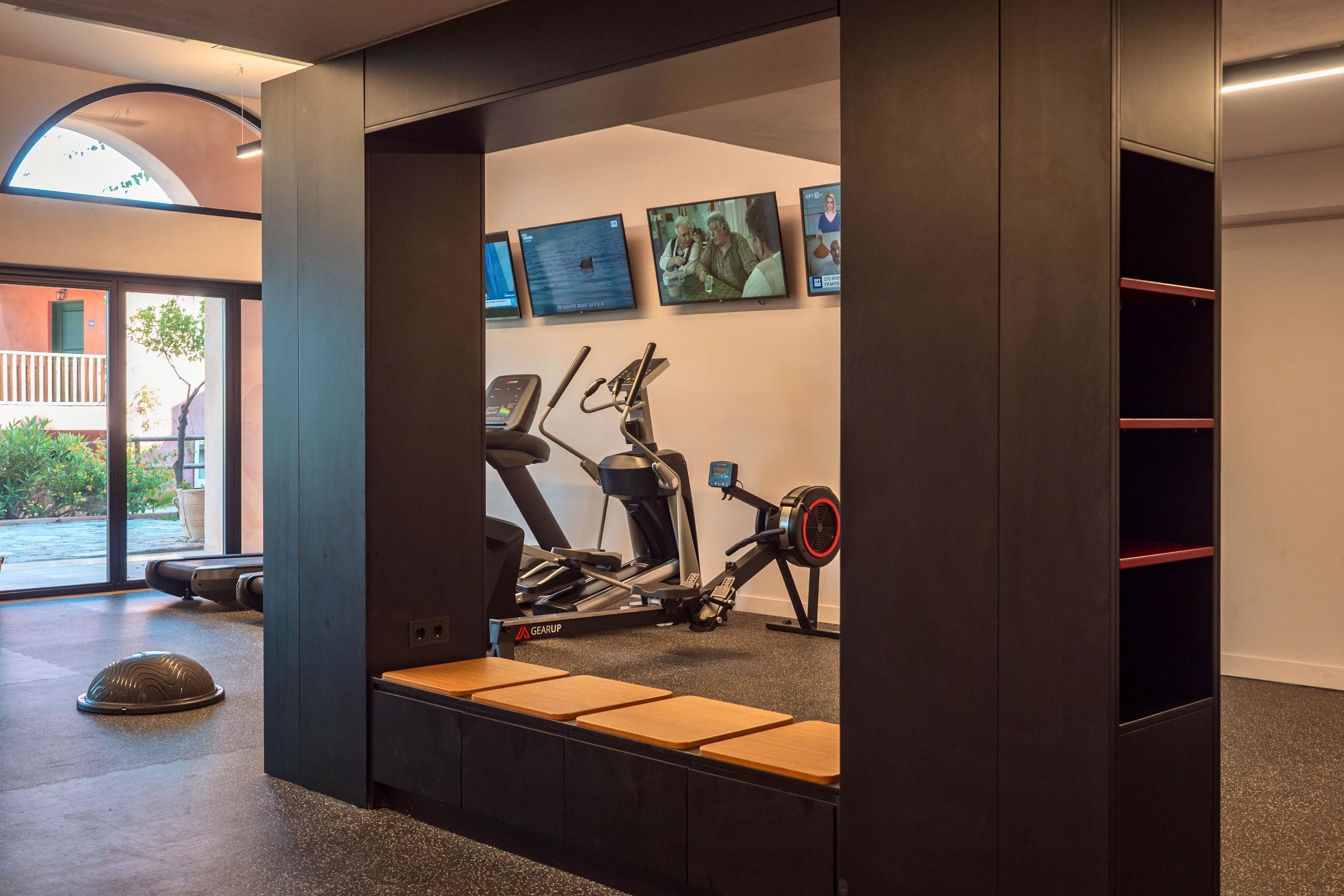 Een moderne fitnessruimte met cardioapparatuur, loopbanden en hometrainers. Er zijn wandmontageschermen die content tonen.