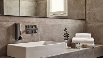 A modern bathroom with a rectangular sink, a wall-mounted faucet, a small potted plant, and neatly stacked towels.