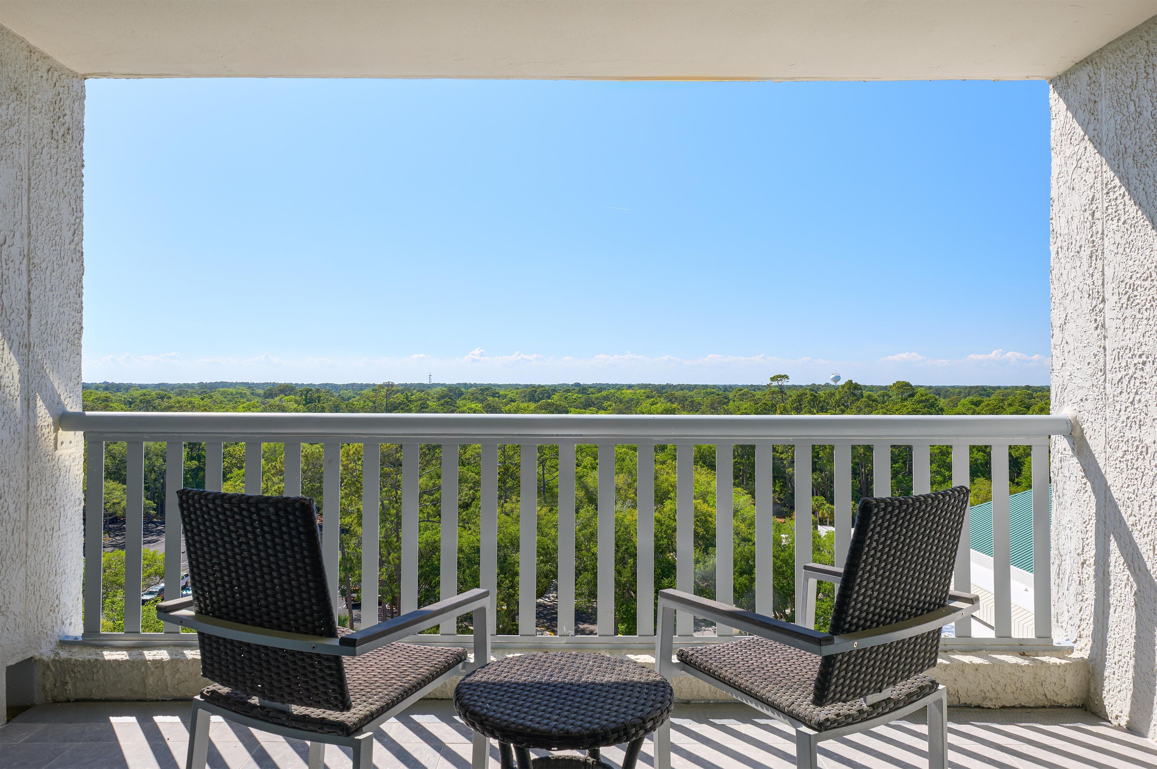 A balcony with two wicker chairs and a small table, overlooking a lush green landscape.
