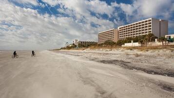 A beachside hotel with a large building, sandy beach, and two cyclists.