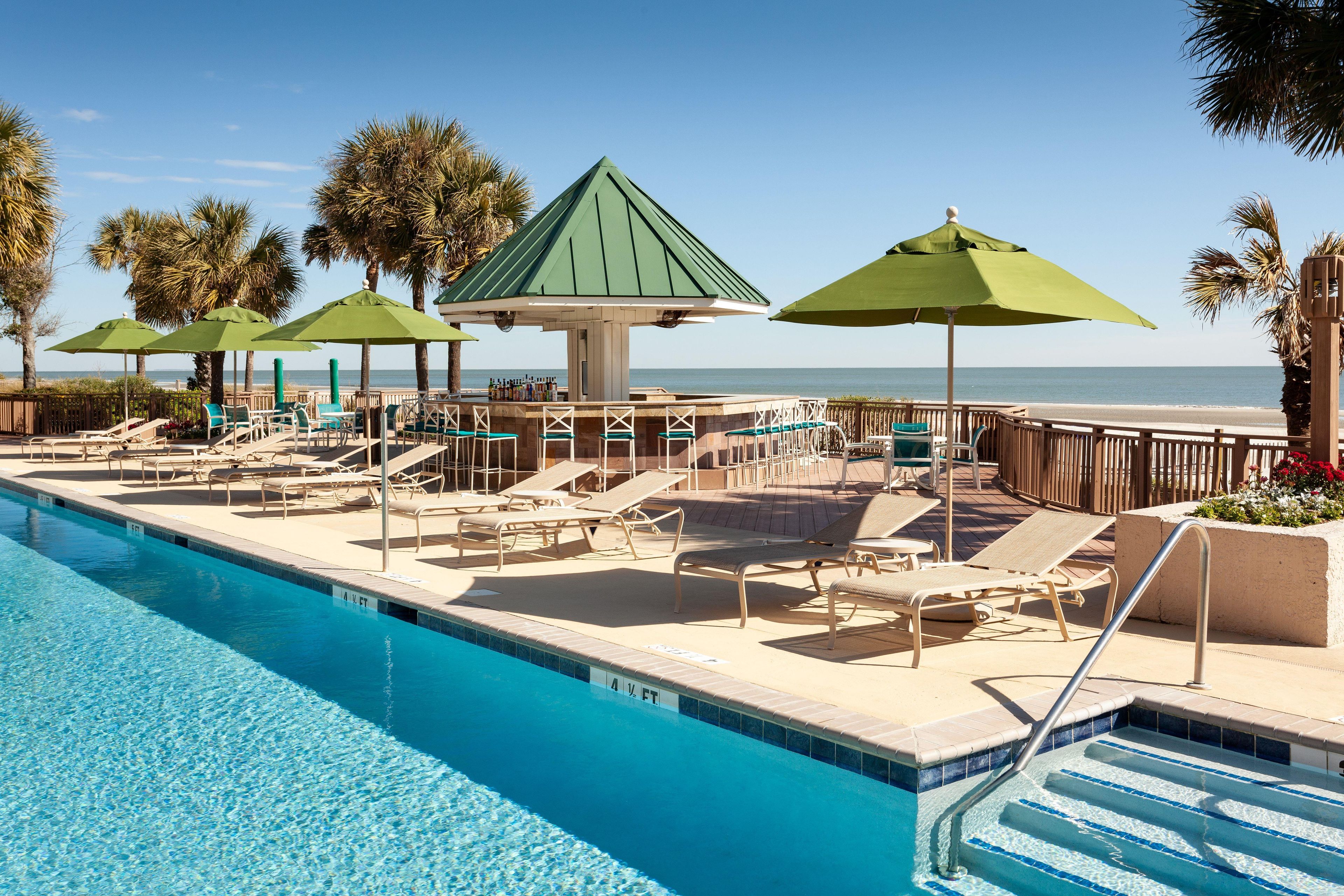 A poolside area with lounge chairs, umbrellas, and a view of the ocean.