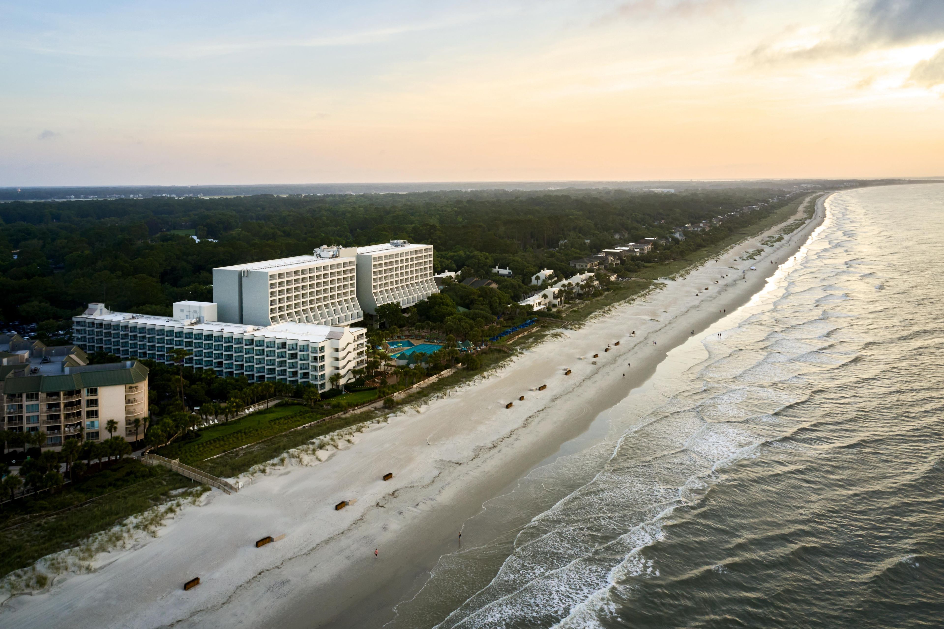 A coastal hotel with multiple buildings, a sandy beach, and the ocean.