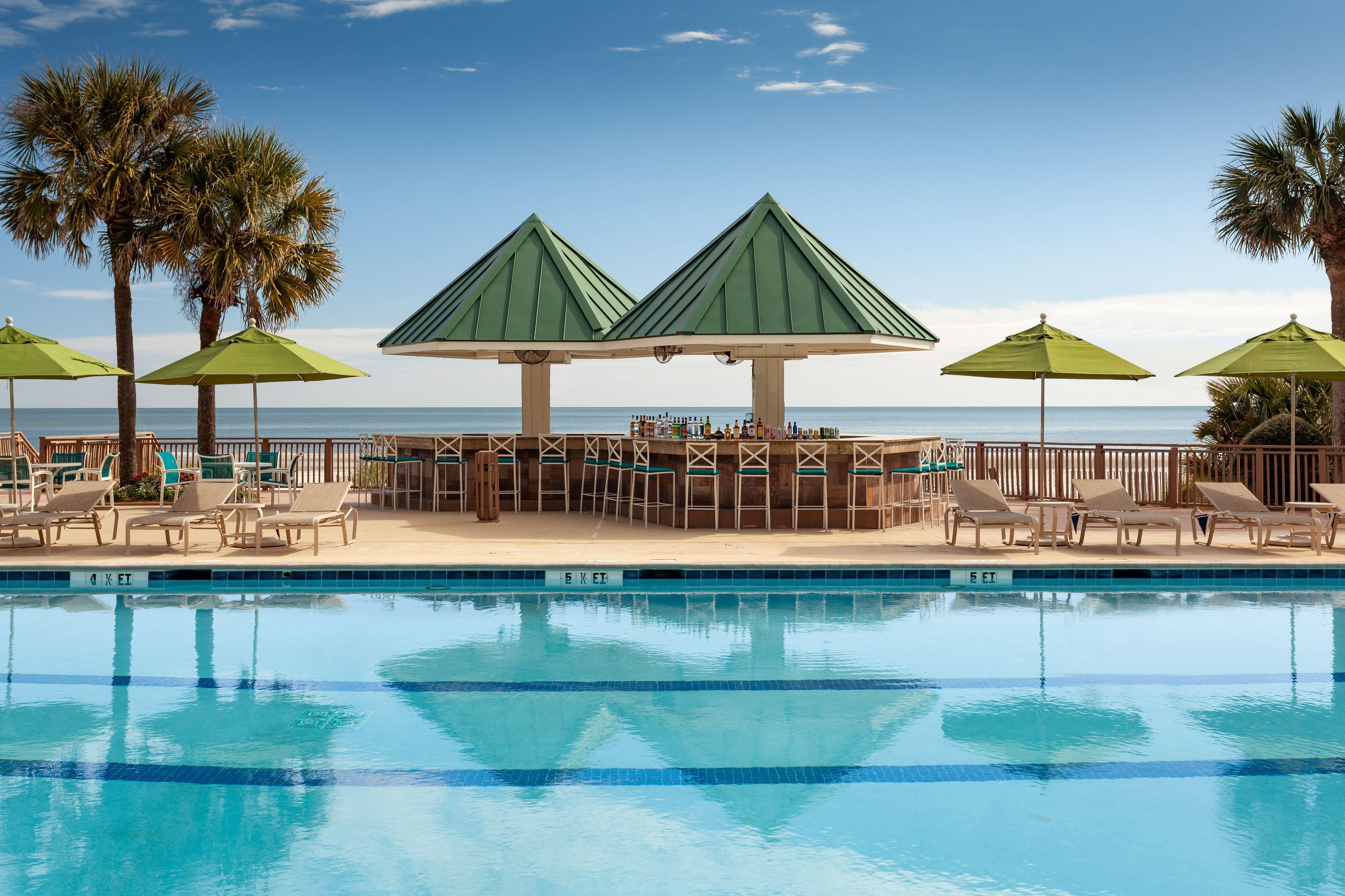 A poolside area with lounge chairs, umbrellas, and a bar area with bottles.