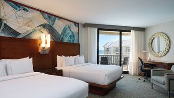 A hotel room with two beds, a desk, a chair, a large window with a view, and a decorative wall piece.
