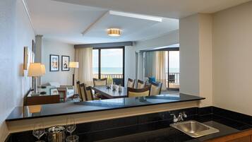 A hotel room with a dining area, a view of the sea, a large mirror, and a kitchen with a sink.