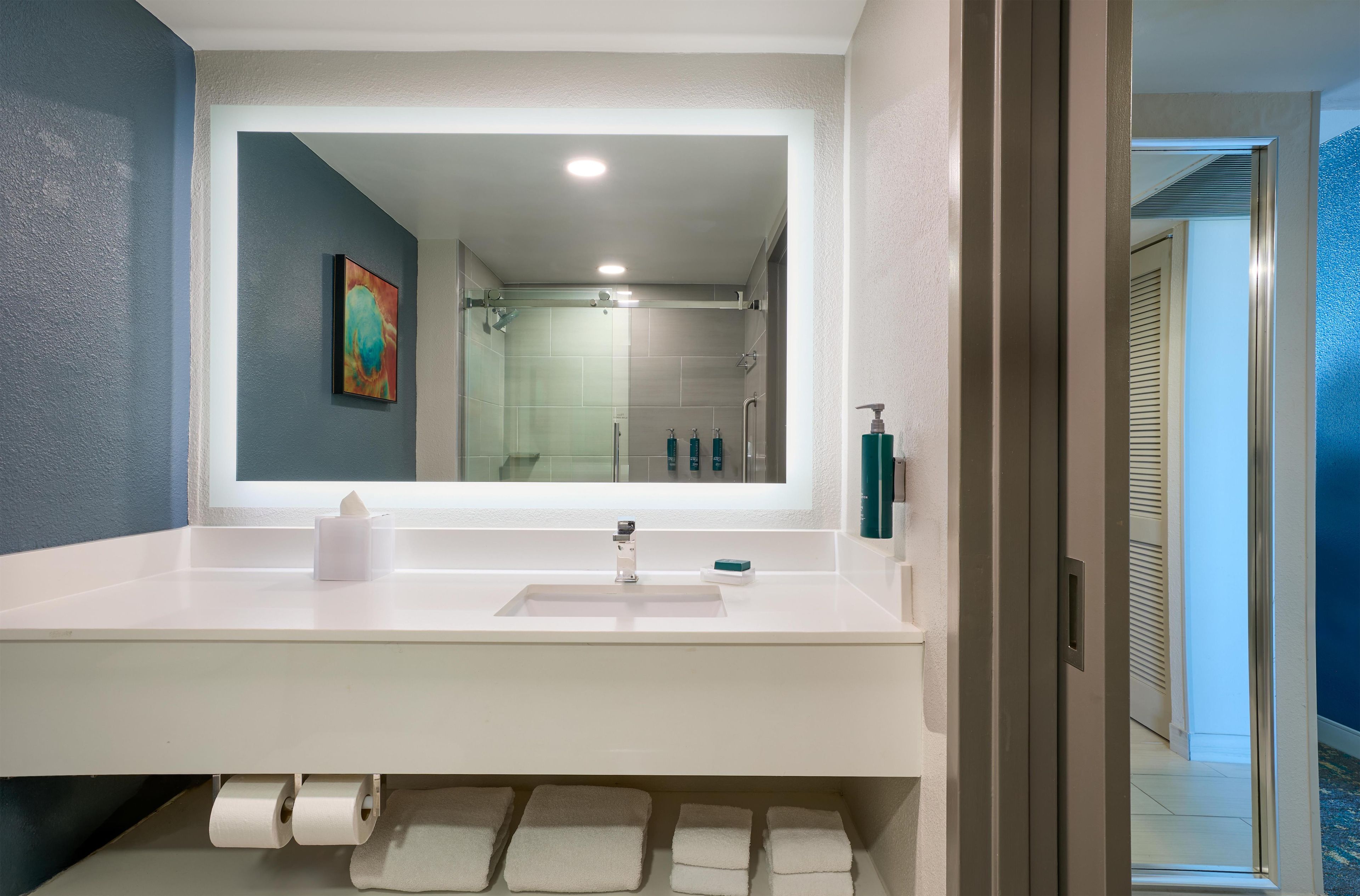 A modern bathroom with a large mirror, white sink, and a shower area visible through the glass door.