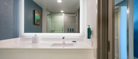 A modern bathroom with a large mirror, white sink, and a shower area visible through the glass door.