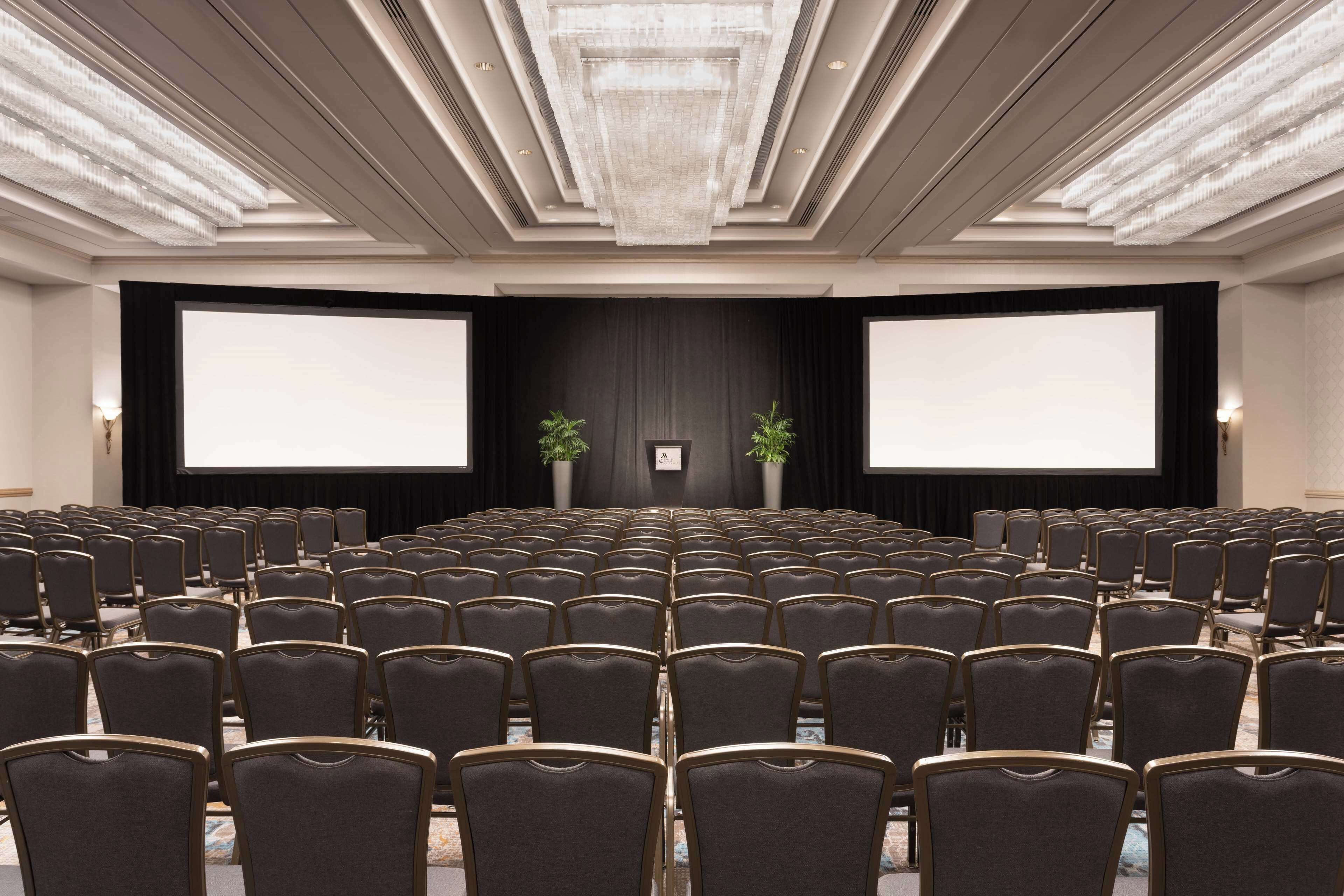 A conference room with rows of chairs, a large screen, and a chandelier.