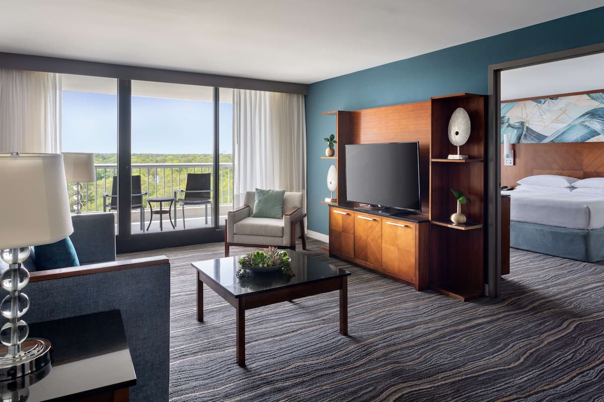 A hotel room with a balcony, a TV, a sofa, a coffee table, and a bed.