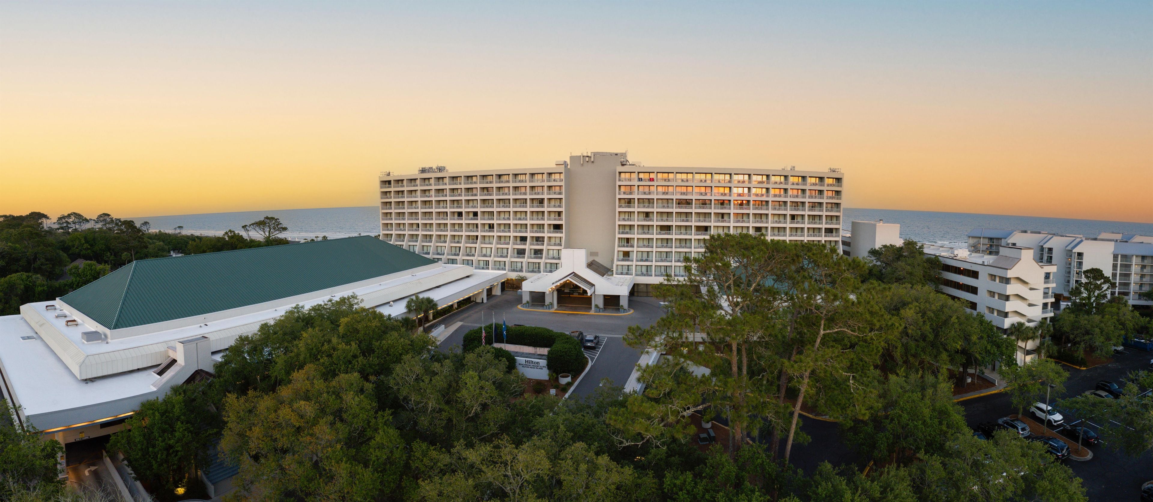 A large hotel with multiple floors, a parking area, and a view of the ocean.