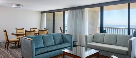 A hotel room with a seating area, a dining table, and large windows with a view.