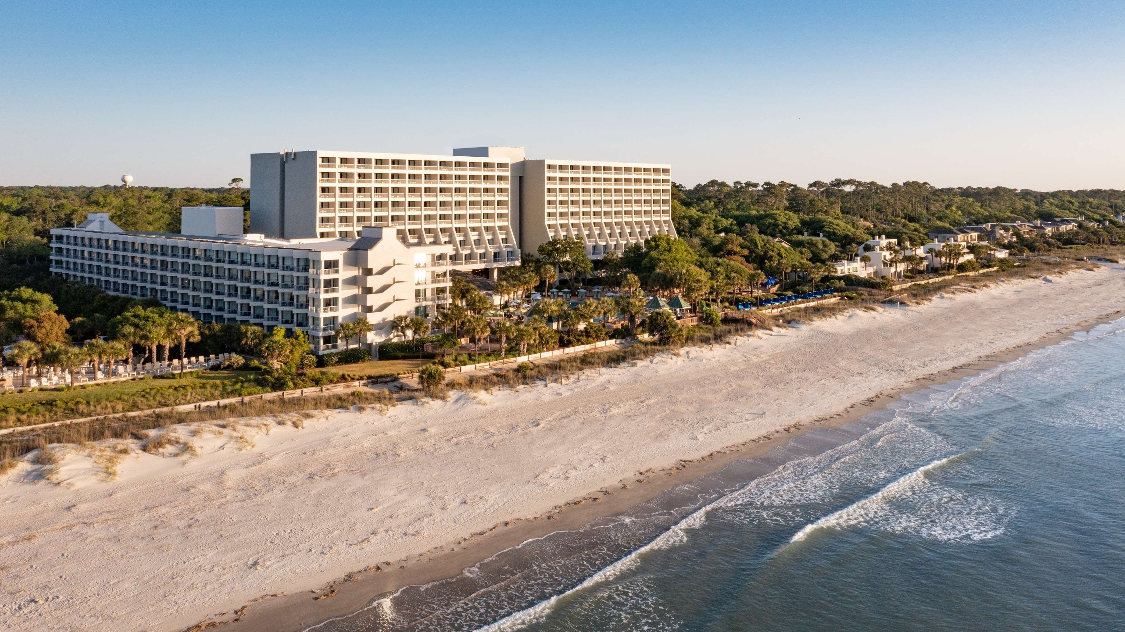 A beachfront hotel with multiple buildings, a sandy beach, and a clear view of the ocean.