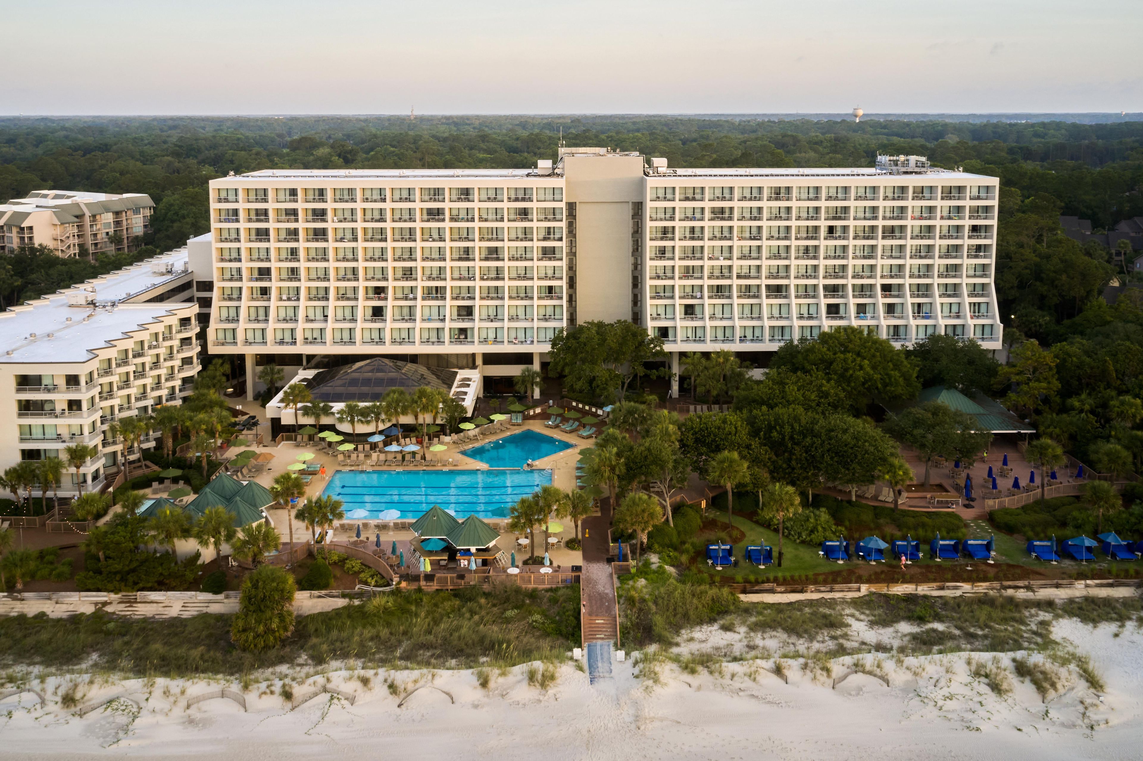 Een groot hotel met meerdere verdiepingen, een zwembad en een strand.