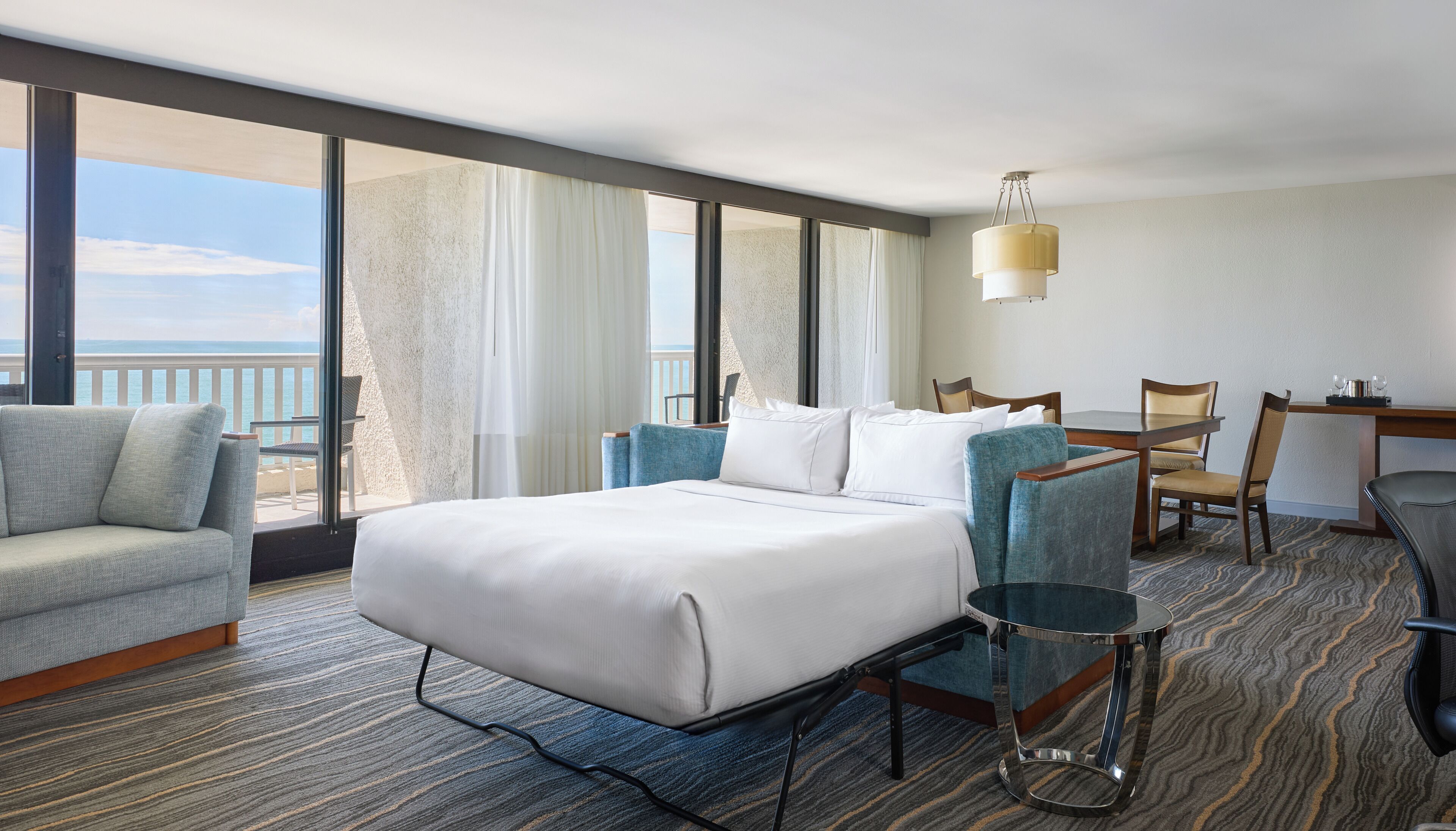 Hotelkamer met een groot bed, een zithoek met een tafeltje en uitzicht op de oceaan.