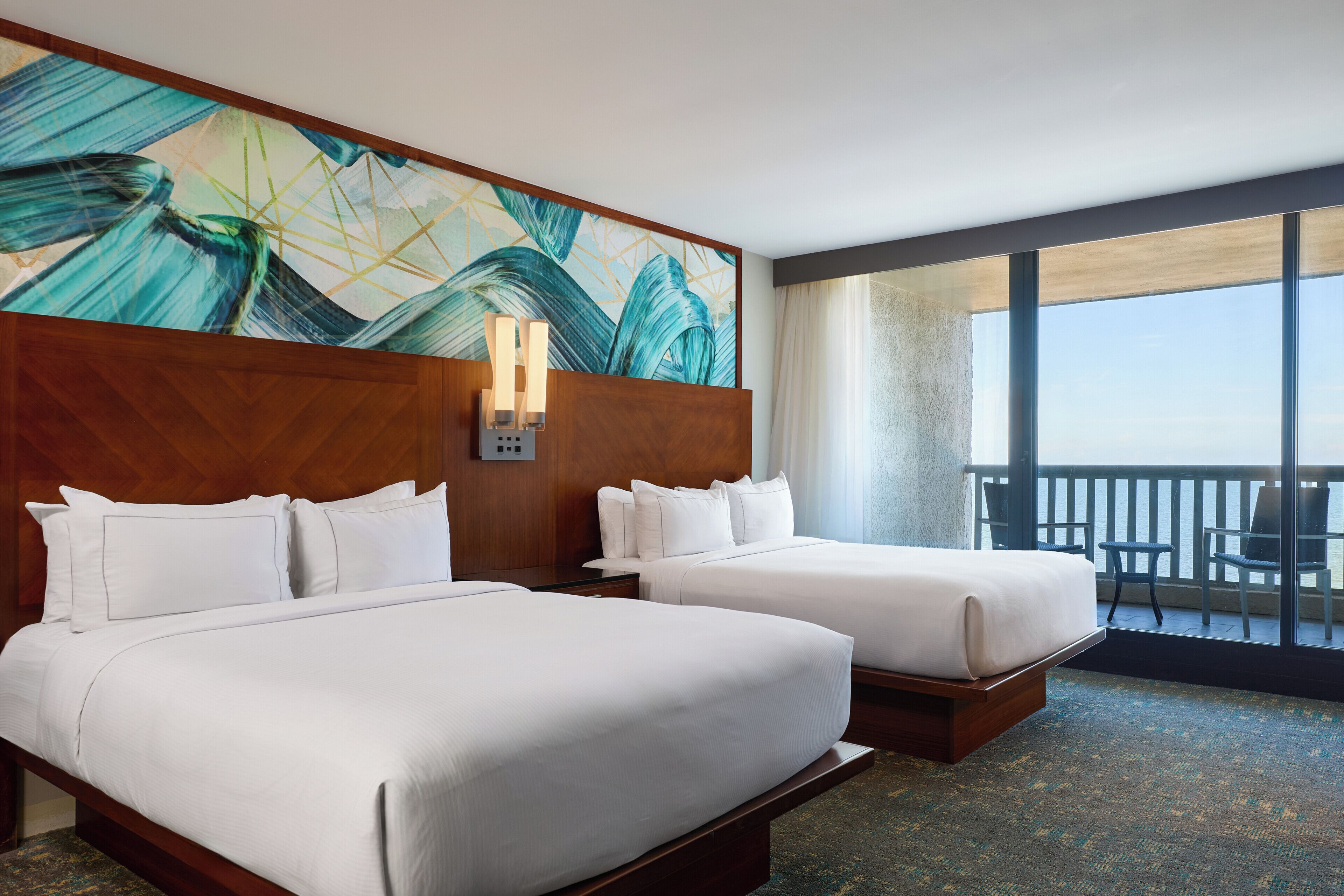 A hotel room with two beds, a large window, and a view of the ocean.