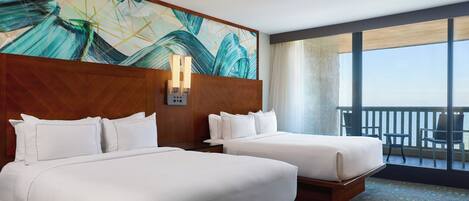 Habitación de hotel con dos camas, un ventanal grande y vista al océano.