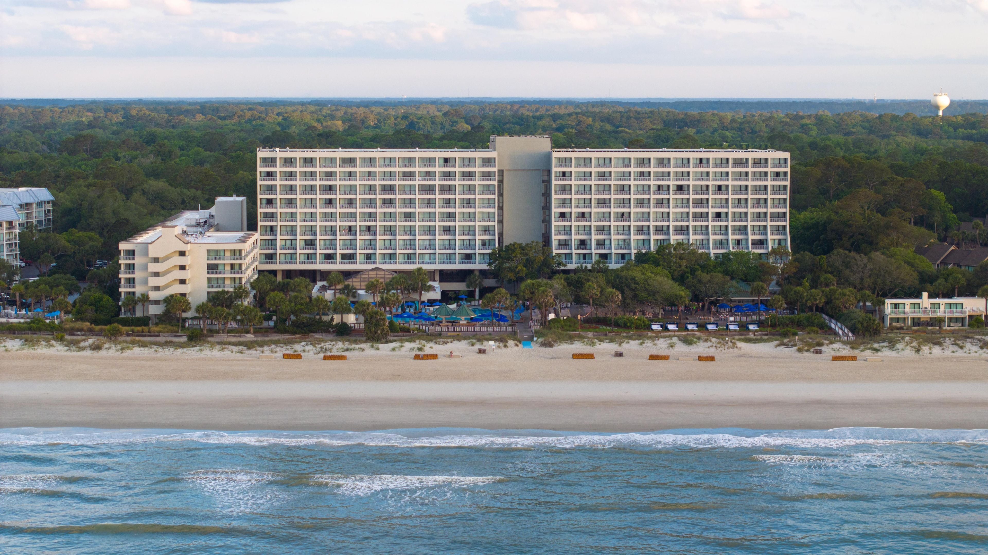A beachfront hotel with multiple floors, a pool area, and a view of the ocean.