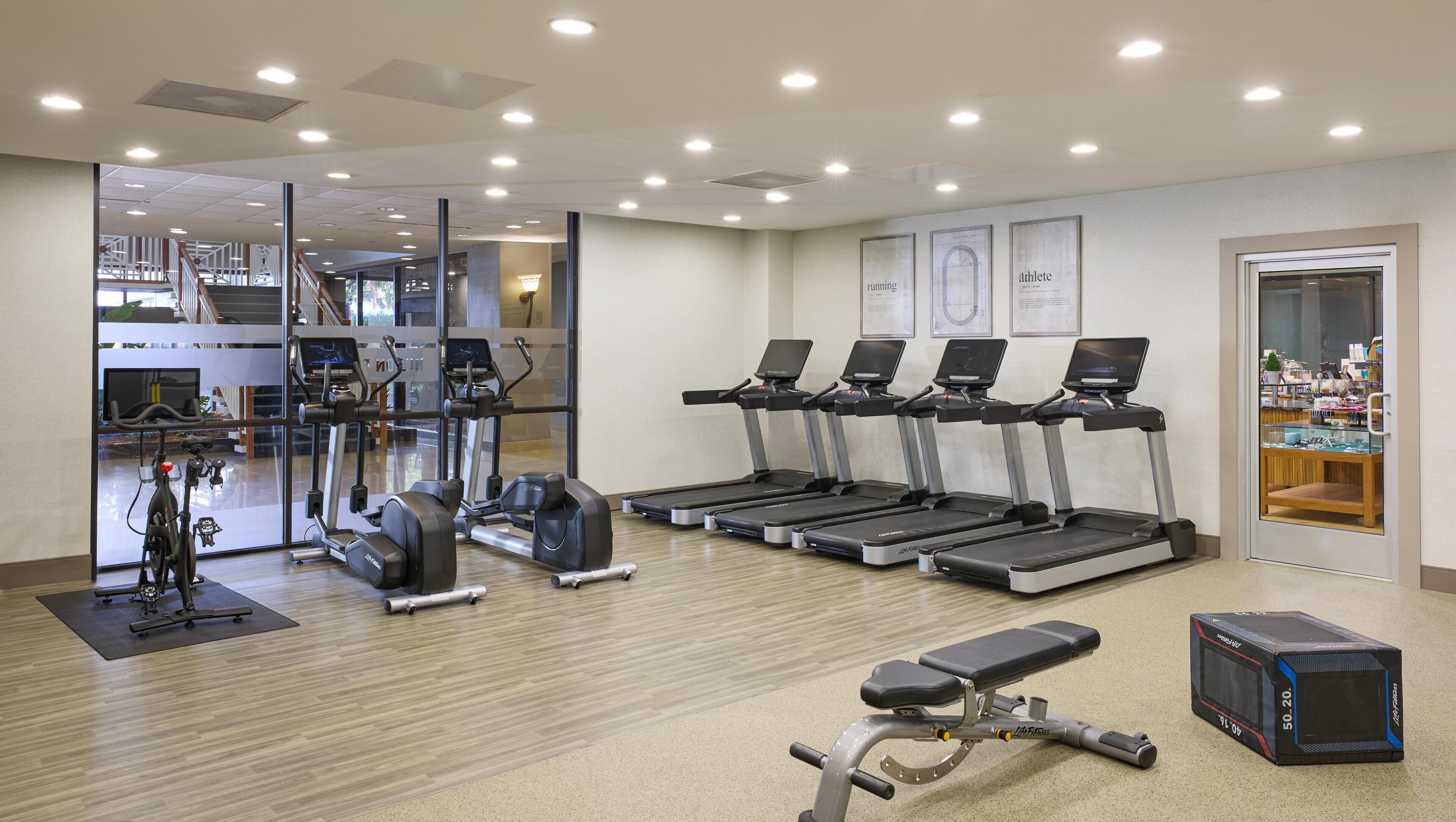 Een fitnessruimte met loopbanden, elliptische trainers en een gewichtbank.