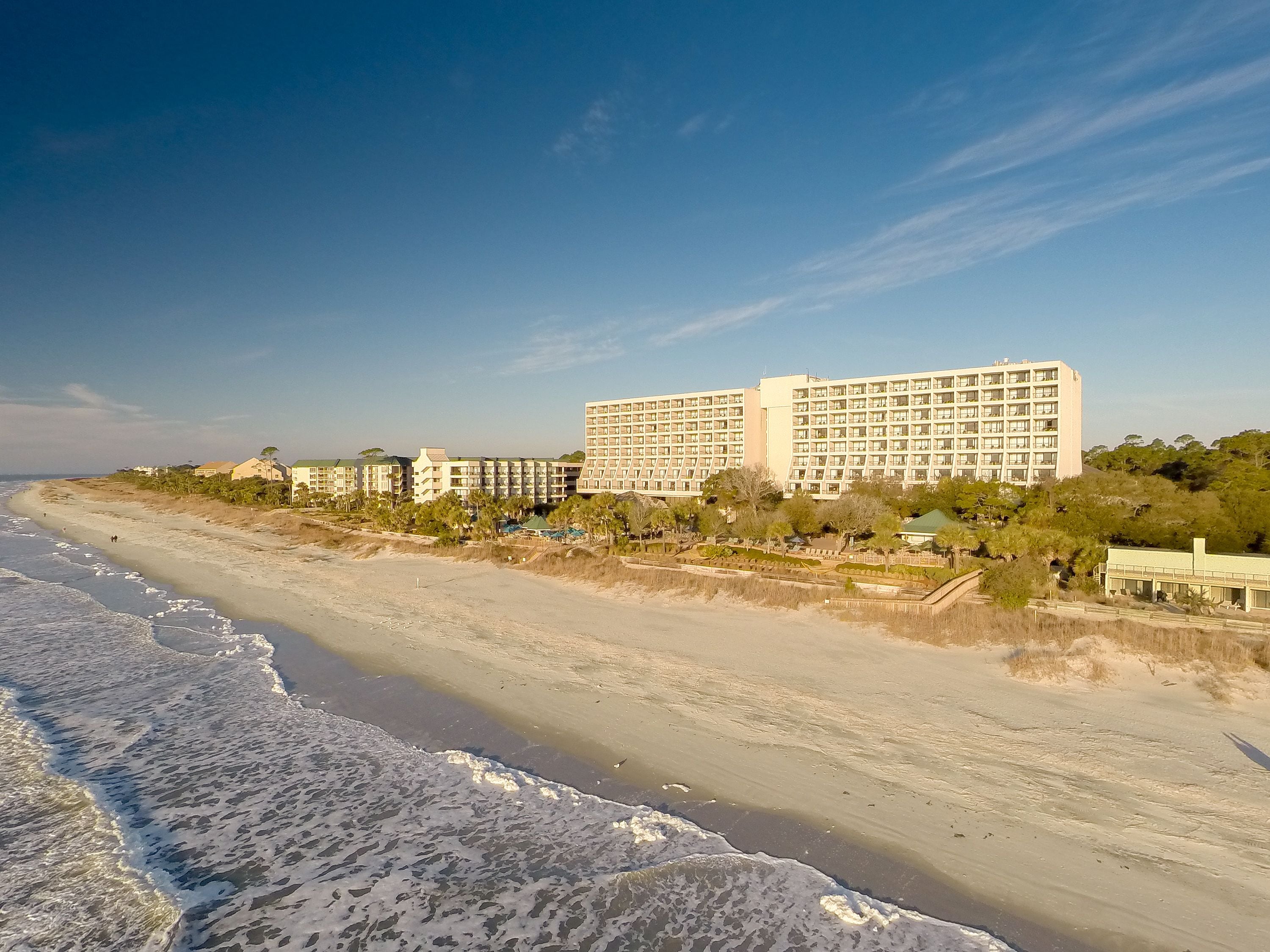 A beachfront hotel with multiple buildings, a sandy beach, and a clear sky.