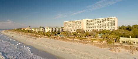 A beachfront hotel with multiple buildings, a sandy beach, and a clear sky.