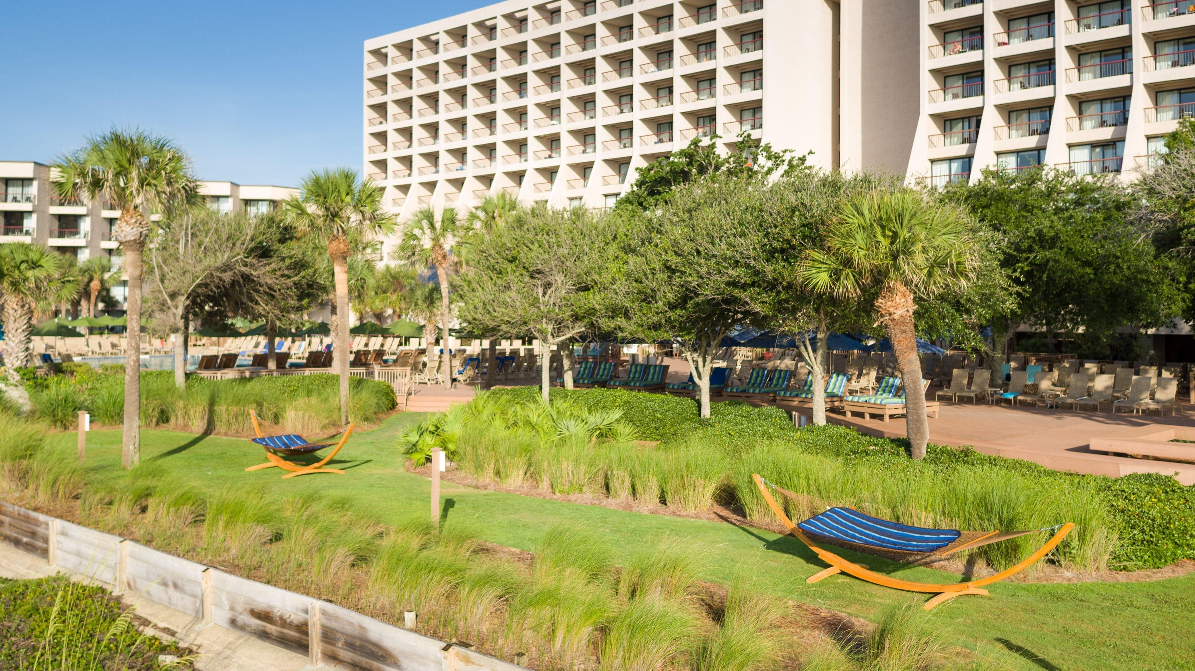 A hotel with a modern building, outdoor seating area with chairs, and a well-maintained garden.