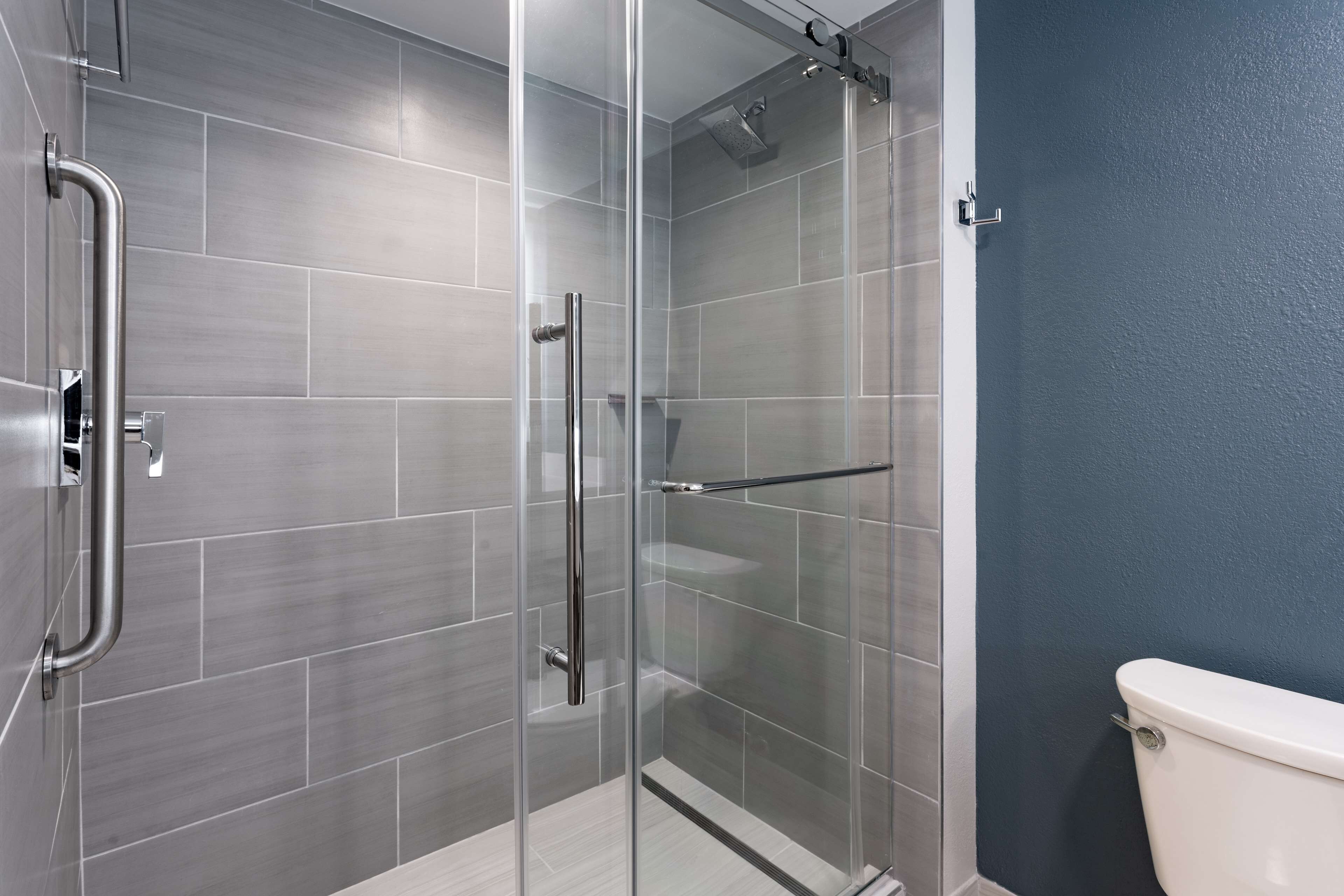 A modern bathroom with a glass shower enclosure, grey tiles, and a white toilet.