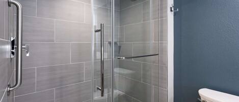 A modern bathroom with a glass shower enclosure, grey tiles, and a white toilet.