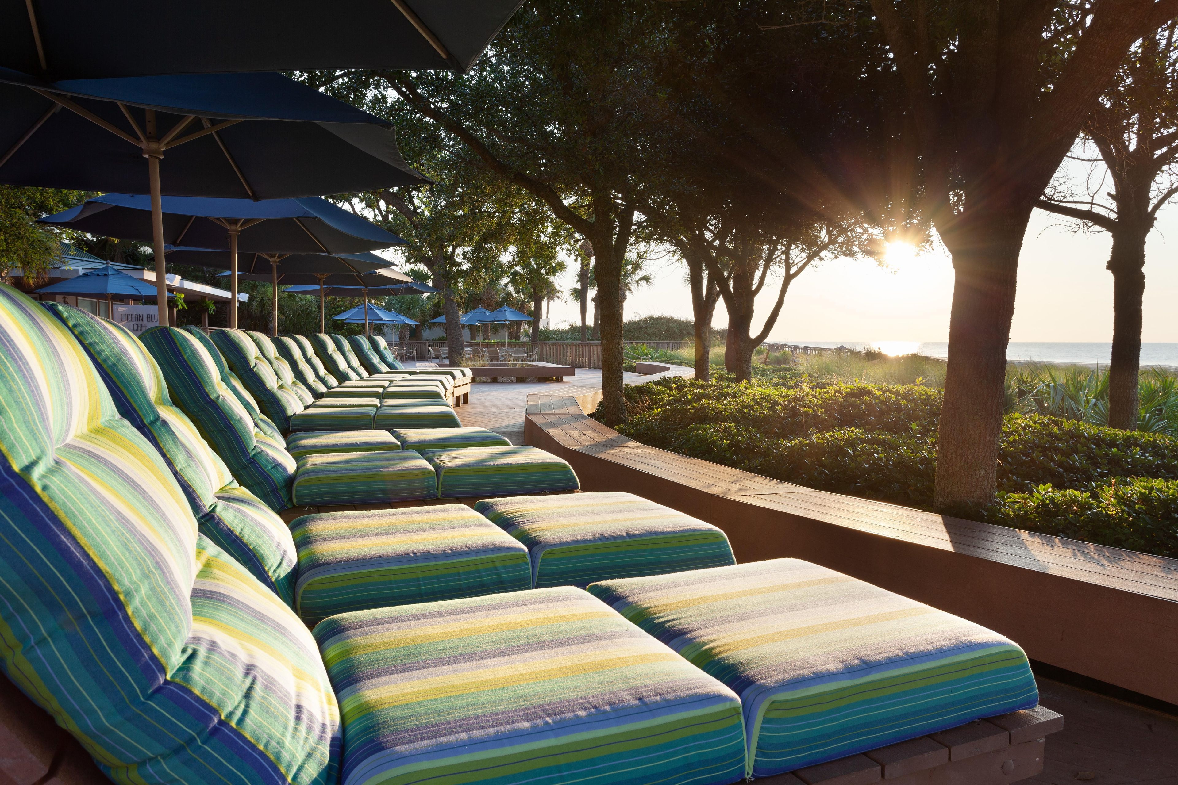 Une rangée de chaises longues à rayures, placées sous des parasols, avec une vue sur la mer et les arbres en arrière-plan.
