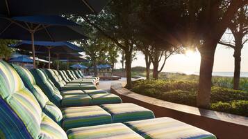 Une rangée de chaises longues à rayures, placées sous des parasols, avec une vue sur la mer et les arbres en arrière-plan.