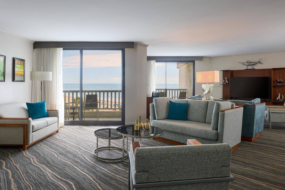 A hotel room with a balcony, a sofa, a TV, and a dining area.