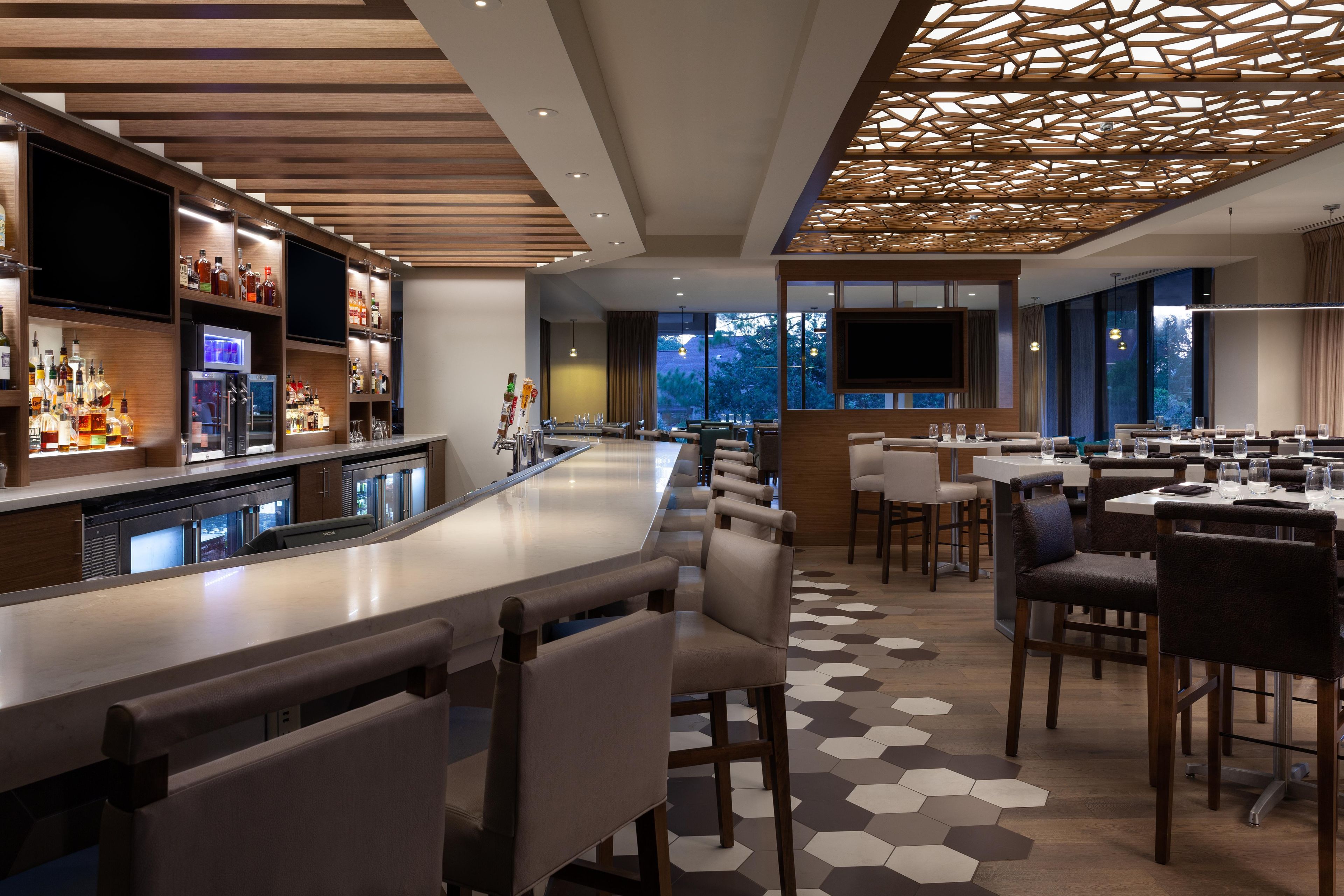 A modern bar area with a long counter, seating, and a patterned ceiling.