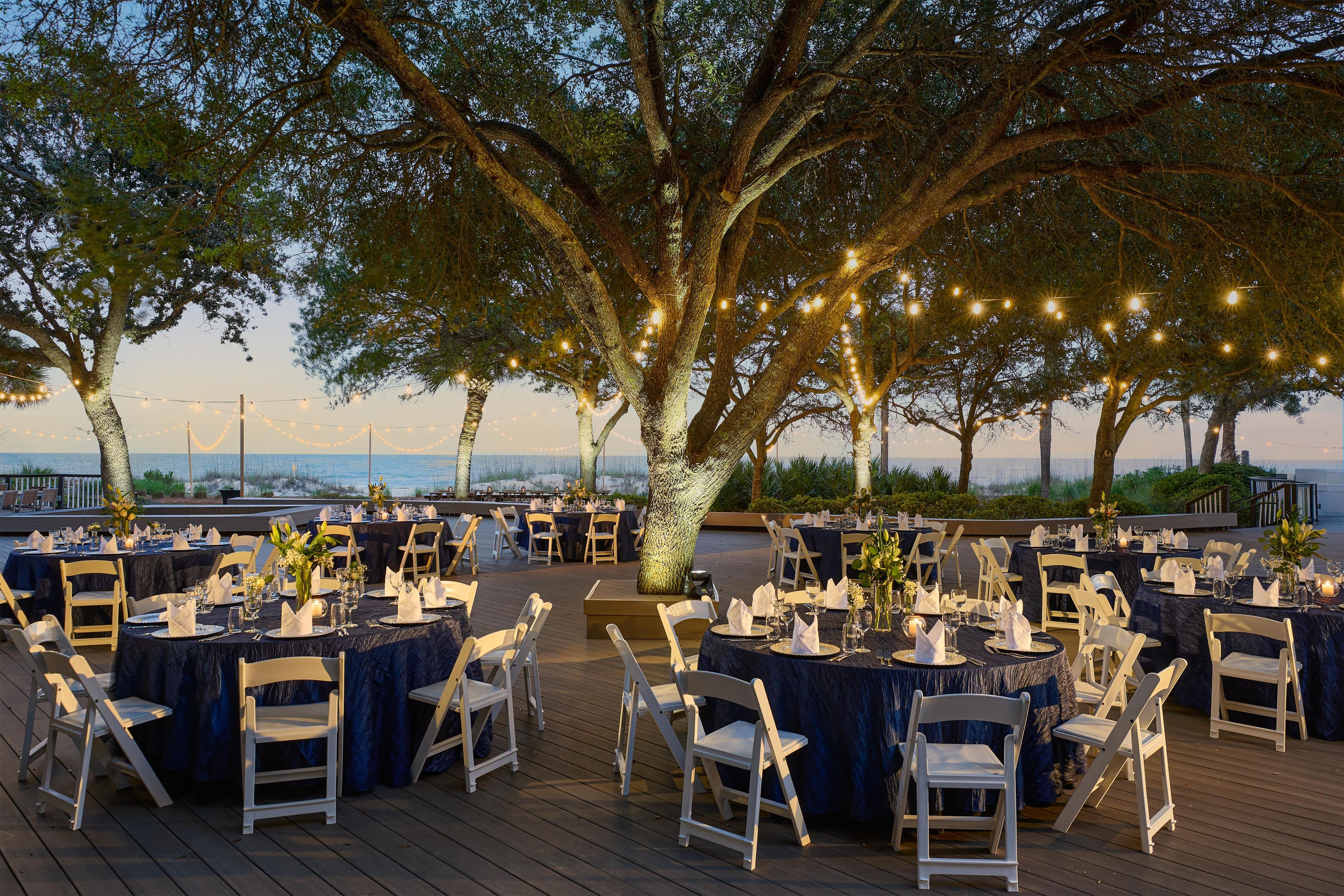 An outdoor event space with round tables, white chairs, and string lights.