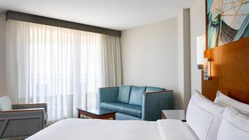 A hotel room with a large bed, a blue armchair, a small table, and a painting on the wall.