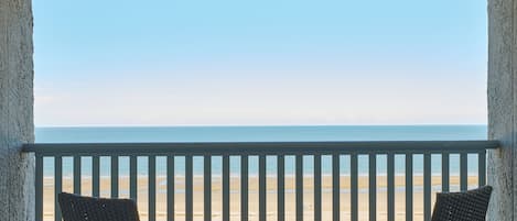 A balcony with two wicker chairs and a small table, overlooking a beach.