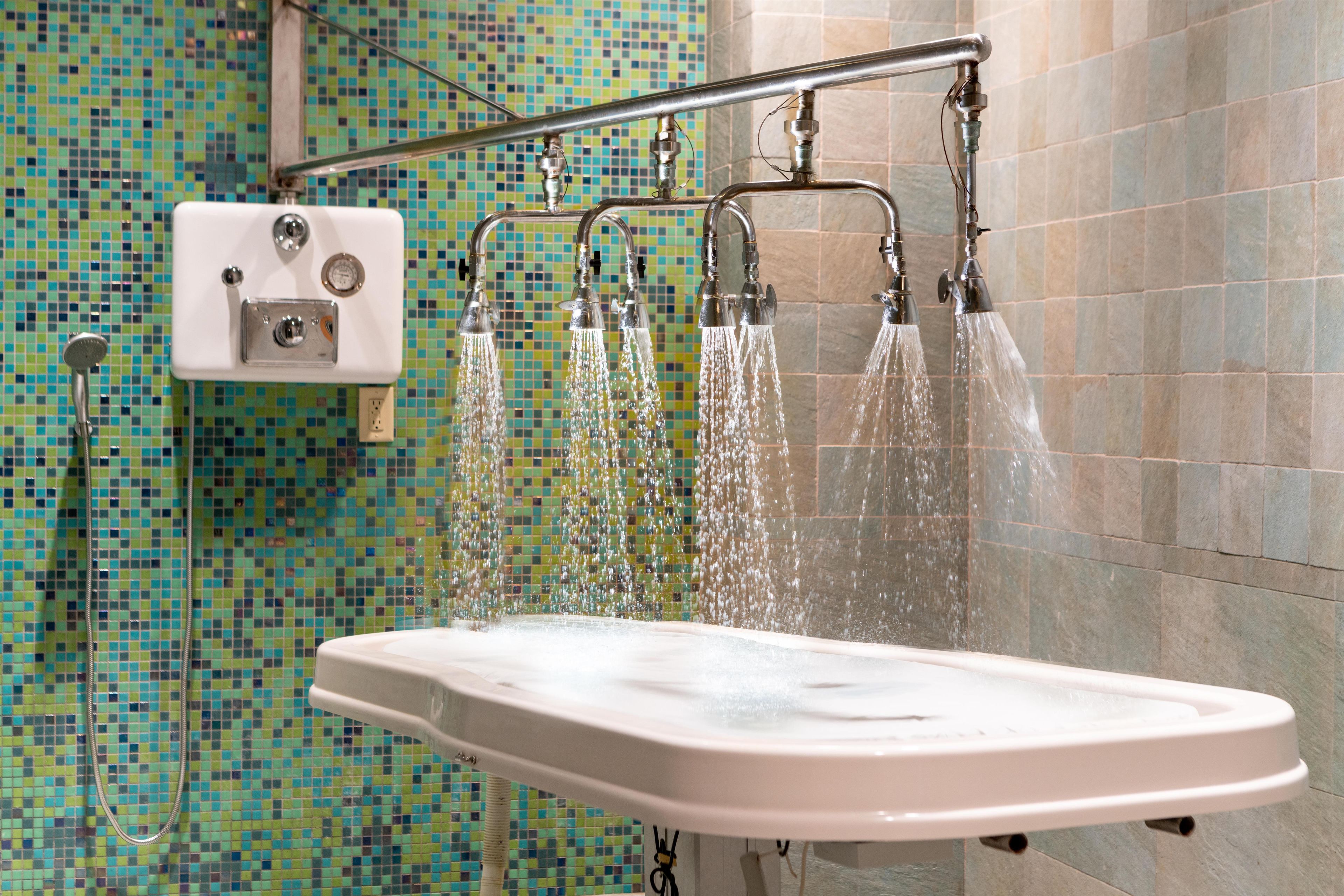 A bathroom with a shower area, a control panel, and a tiled wall.