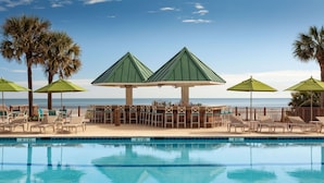 A poolside area with lounge chairs and umbrellas, a bar area, and a view of the ocean. - Hilton Beachfront Resort & Spa Hilton Head Island (Hilton Head Island)