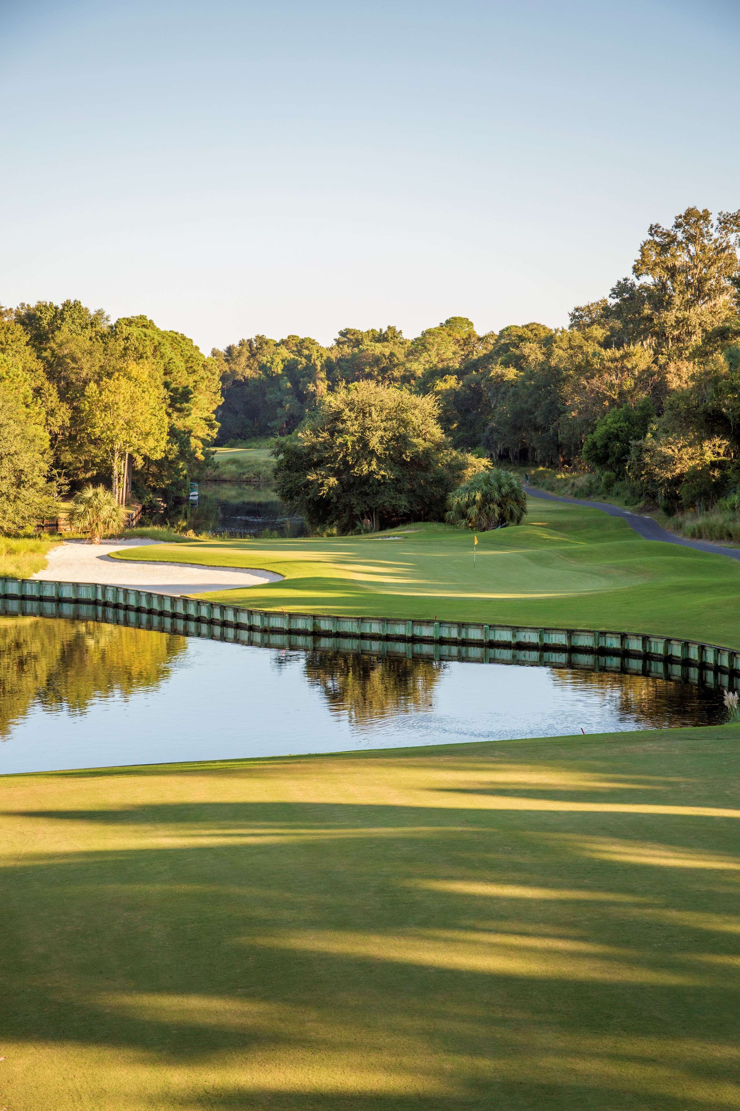A golf course with a pond, sand bunkers, and a flag on the green.