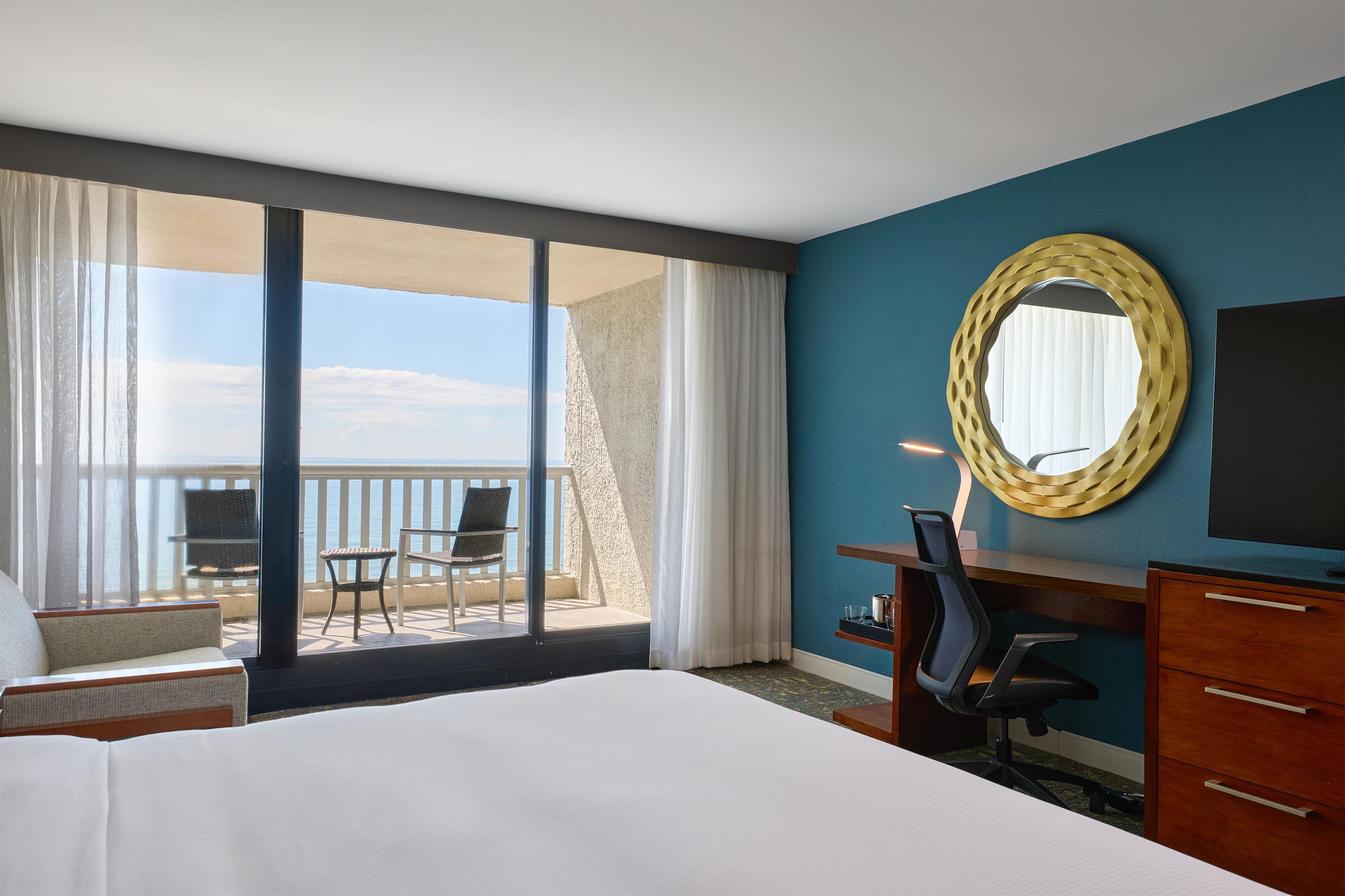 Une chambre d’hôtel avec un grand lit, un bureau, une chaise, une télévision et un balcon avec vue sur la mer.